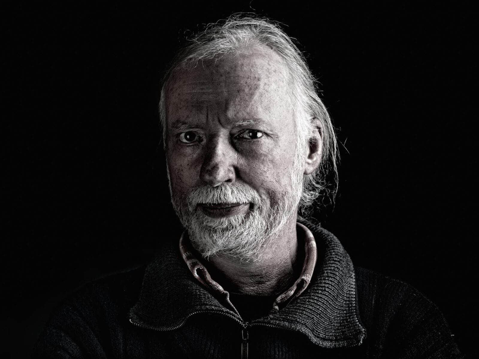 Porträt eines Mannes mit selbstbewussten Blick, vor schwarzen Hintergrund