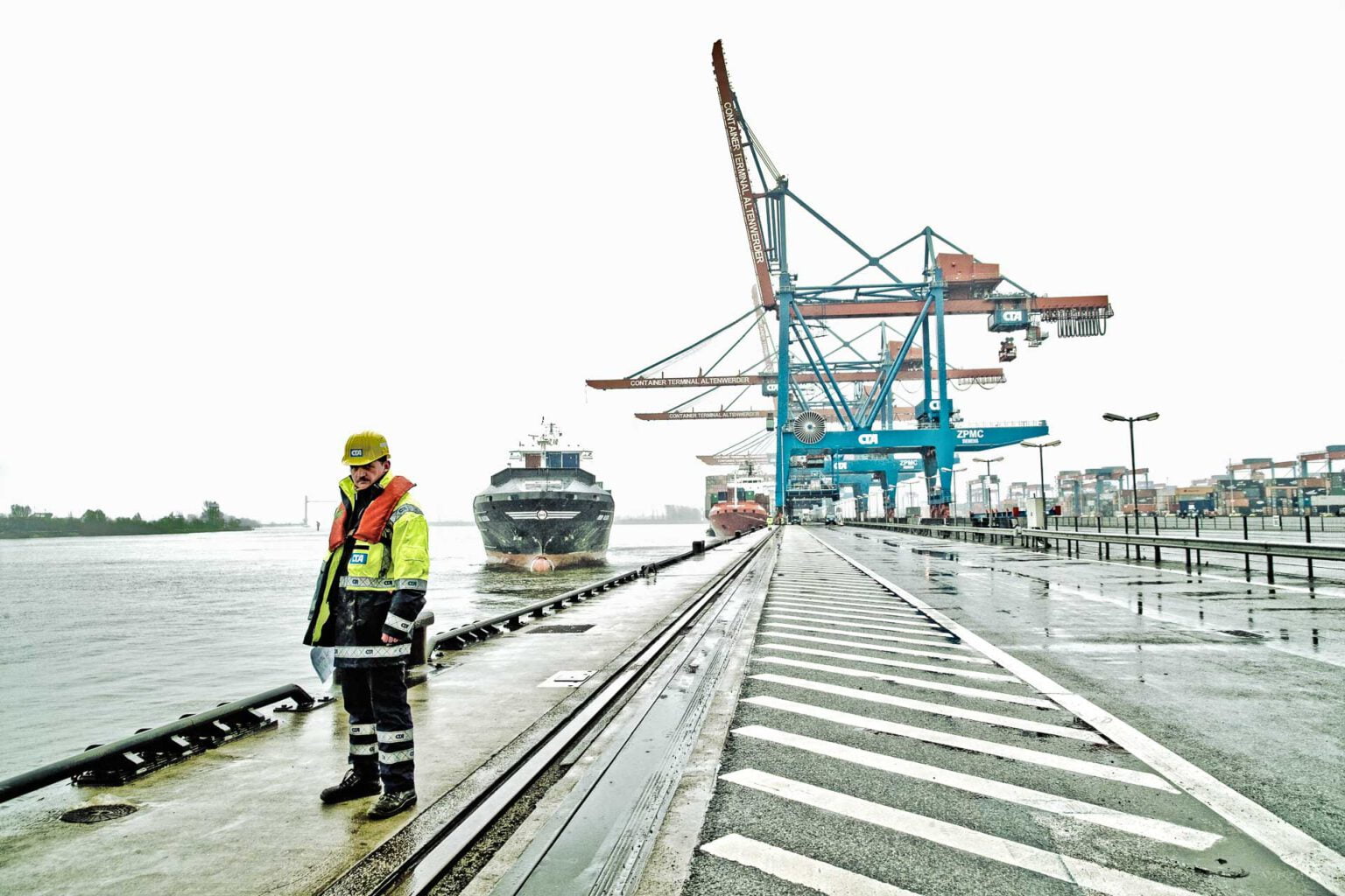 Hafenarbeiter vor Kaianlage mit Schiff, das anlegt.