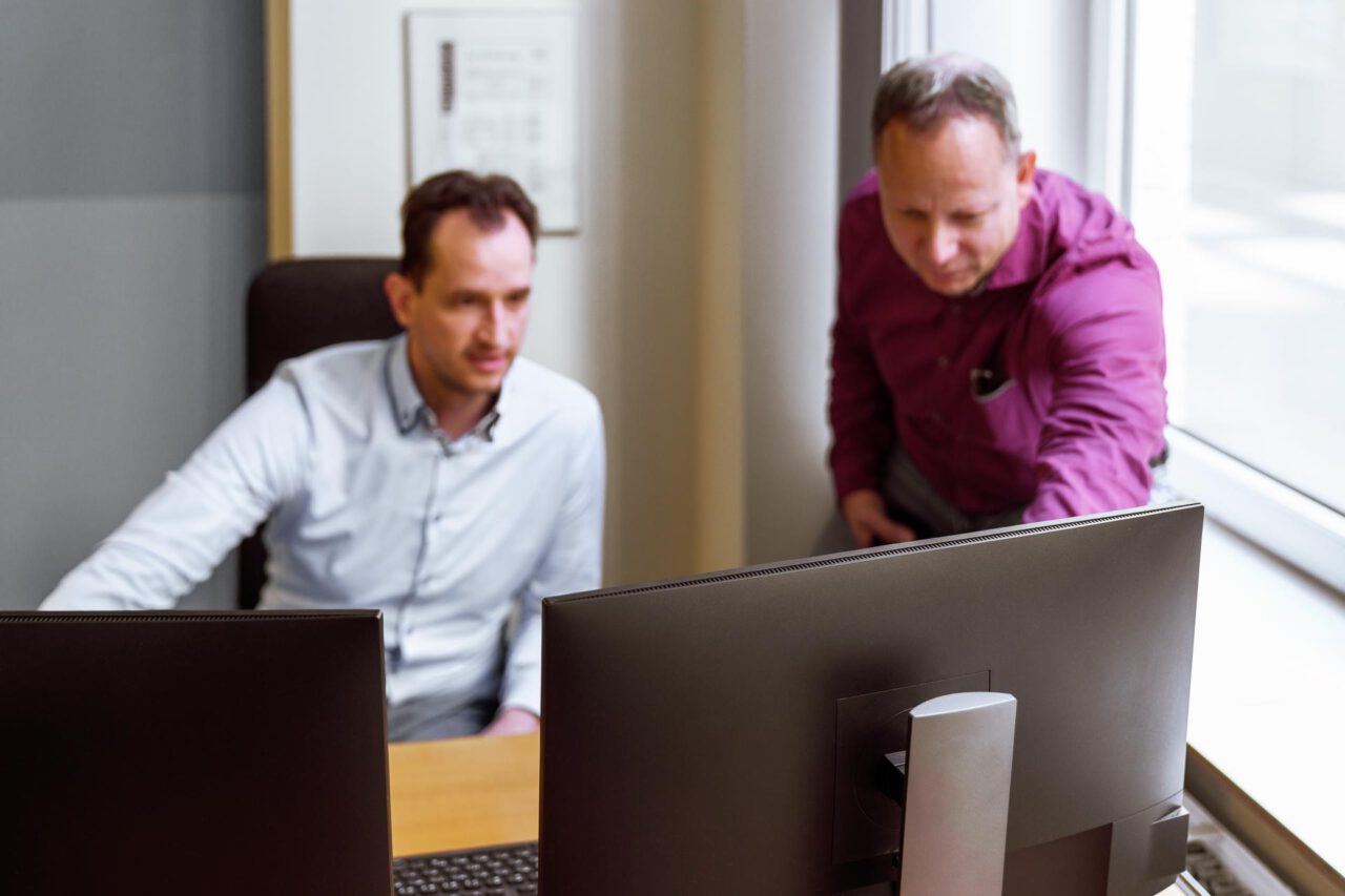Corporatefotografie – Teamwork-Szene mit Mitarbeitern am Tisch in modernem Büro, authentische Darstellung von Zusammenarbeit im Unternehmen