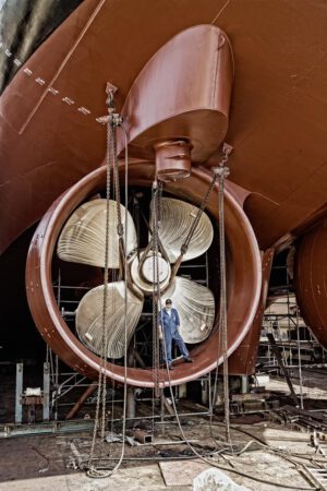 industrie-schiffsschraube-werftarbeiter Arbeiter steht neben der Schiffsschraube eines Schiffes das sich im Dock befindet