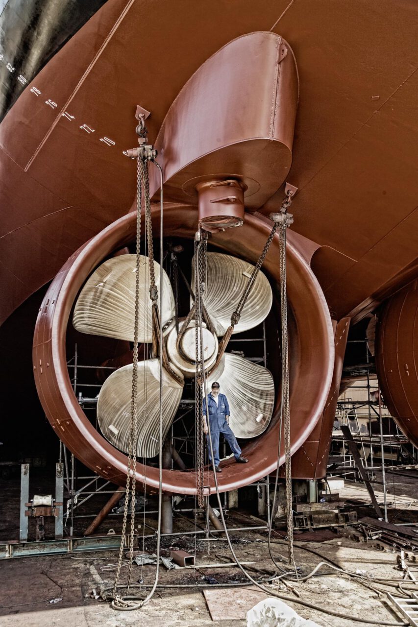 Arbeiter steht neben der Schiffsschraube eines Schiffes das sich im Dock befindet