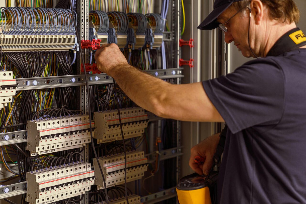 Elektrotechnik Fotografie – Mitarbeiter misst Werte im Schaltschrank, präzise Darstellung industrieller Automatisierungstechnik und Steuerungssysteme