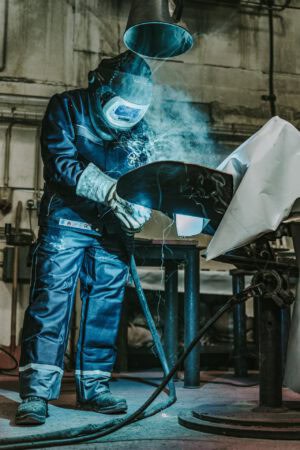 Schweißer bei Metallarbeiten in der Industrie, Schutzkleidung und Funkenflug sichtbar.