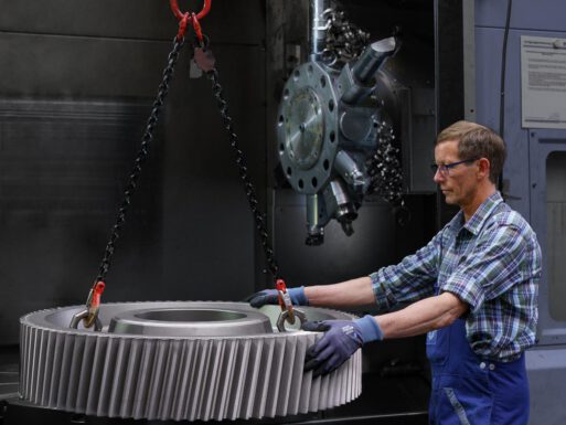 Maschinenbau-Fotografie – Fertigung eines großen Zahnrades, das von einem Arbeiter aus der Zerspanungsanlage geführt wird.